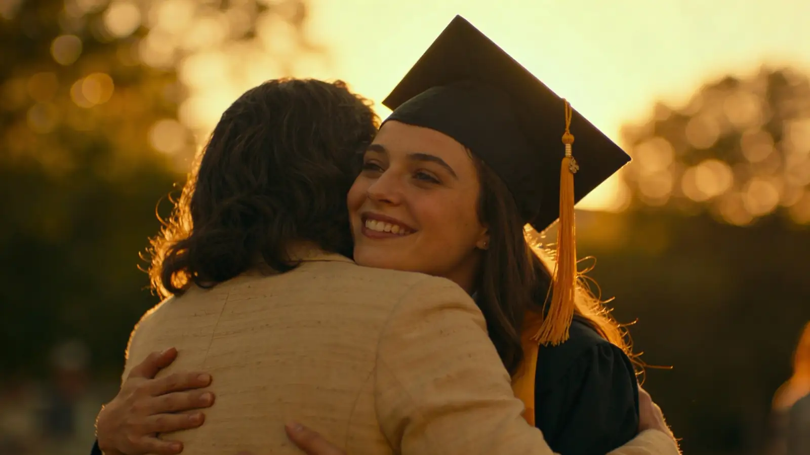 Mother embracing daughter in graduation cap and gown, golden hour light
